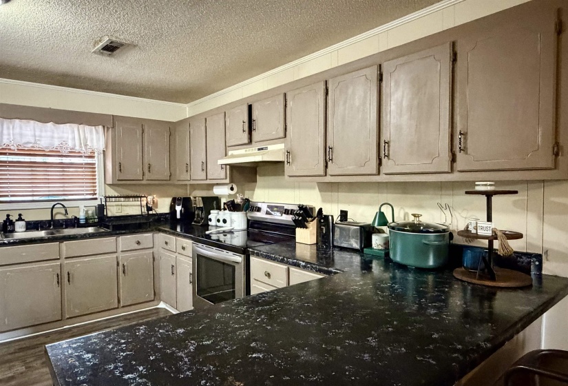 Kitchen featuring a textured ceiling, stainless steel range with electric stovetop, under cabinet range hood, ornamental molding, and a kitchen bar