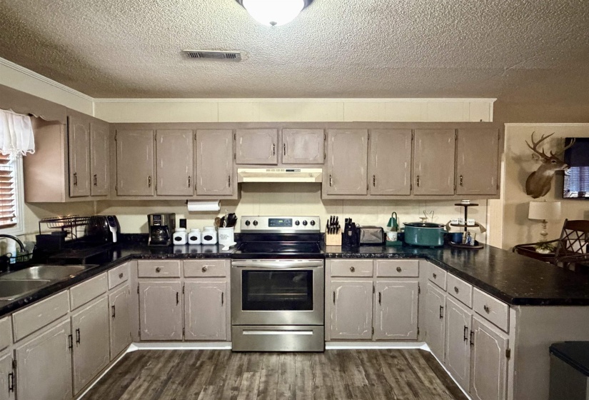 Kitchen with electric stove, dark wood-style flooring, a textured ceiling, under cabinet range hood, and a peninsula