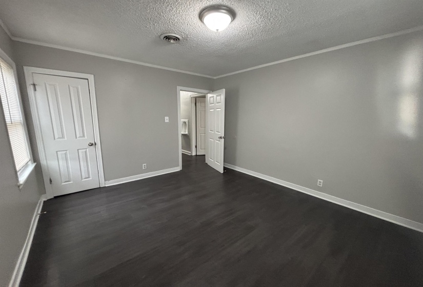 Unfurnished bedroom featuring a textured ceiling, crown molding, dark wood-style flooring, and a closet