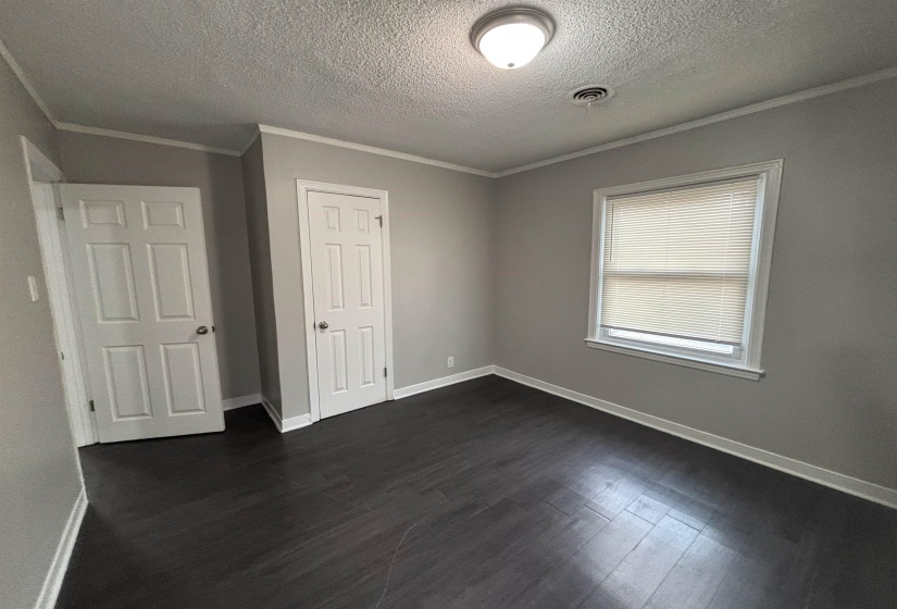 Unfurnished bedroom with a textured ceiling, crown molding, dark wood-style flooring, and a closet