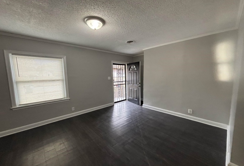 Empty room featuring a textured ceiling, crown molding, and dark wood-style floors