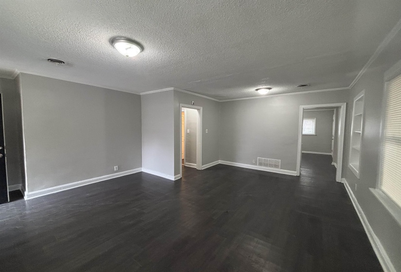 Empty room featuring a textured ceiling, dark wood-type flooring, built in features, and crown molding