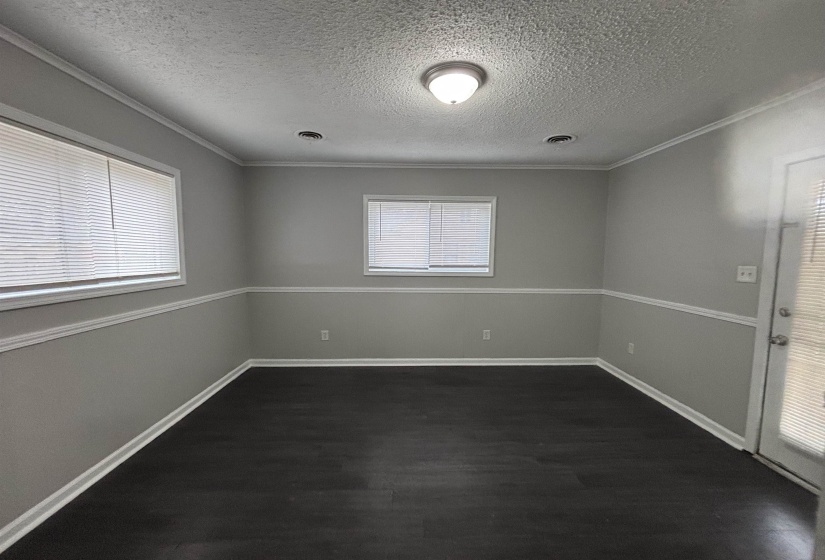 Empty room with healthy amount of natural light, a textured ceiling, dark wood finished floors, and ornamental molding