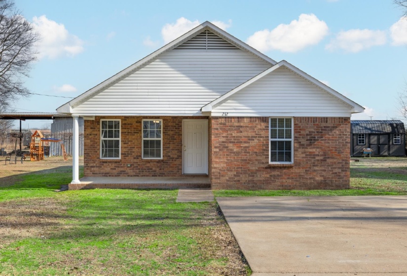 View of front of property with a front yard, a porch, and brick exterior.