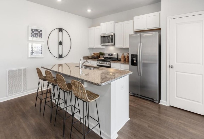 Kitchen featuring appliances with stainless steel finishes, light stone counters, a kitchen breakfast bar, white cabinetry, and an island with sink