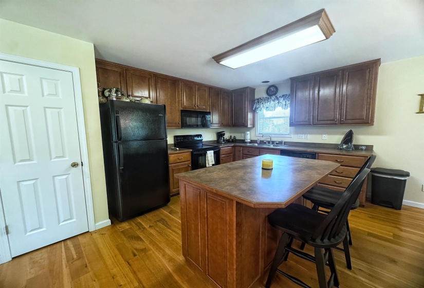 Kitchen featuring an eat-at island, perimeter wood-finish cabinetry, black appliances, and wood-finish flooring