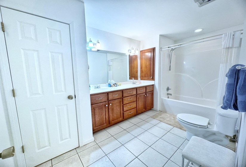 Bathroom featuring a dual vanity with wood cabinetry and white countertops, a mirror spanning both sinks, and a tub/shower combination with a white surround