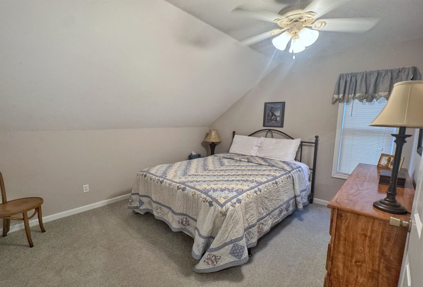 Carpeted room with sloped ceiling, featuring a window with blinds, ceiling fan, and painted walls