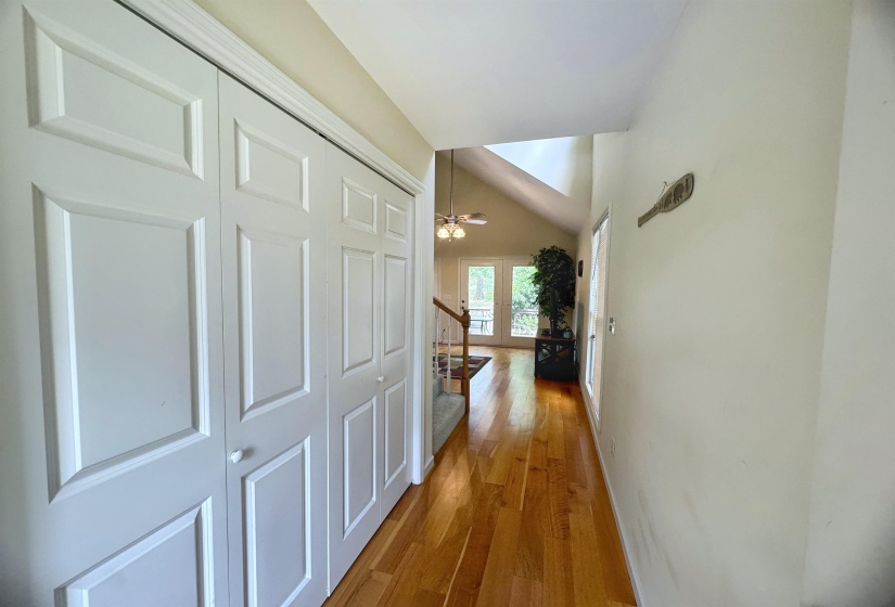 Hardwood flooring extends through a hallway with white bi-fold closet doors, leading to a living area with a vaulted ceiling and French doors