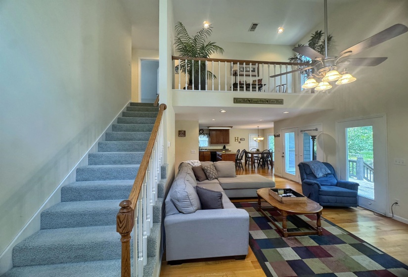 Vaulted ceiling living area featuring hardwood flooring, a ceiling fan with integrated lighting, and multiple exterior doors