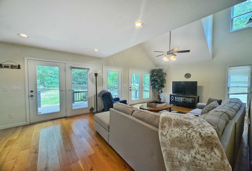 Living area featuring a vaulted ceiling with a ceiling fan, recessed lighting, wood-finish flooring, and multiple glass-paneled French doors opening to an exterior deck