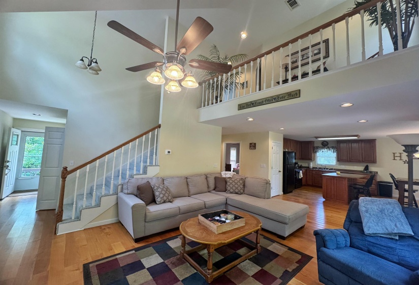 Bright open-concept living area with a lofted second story, hardwood flooring, and a ceiling fan