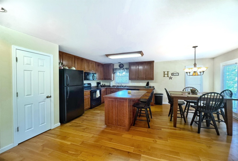 Kitchen and dining area featuring wood-finish flooring, wood cabinetry, black appliances, and a central island with seating