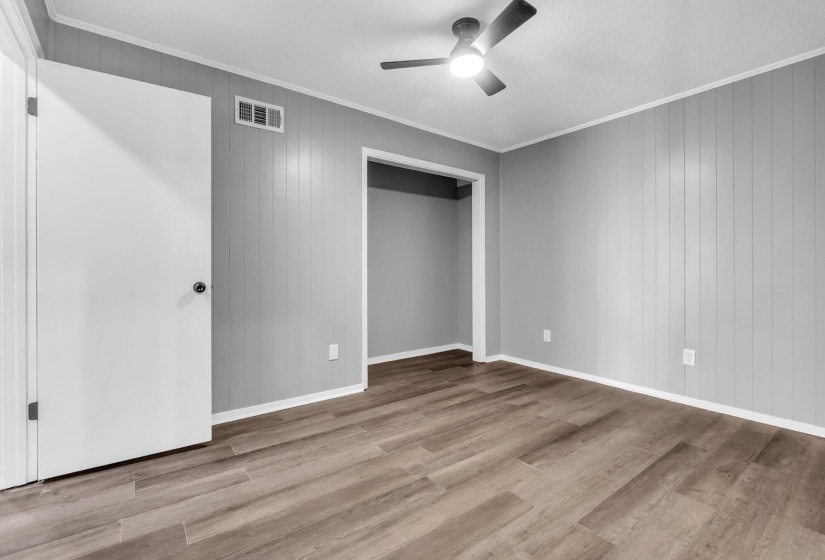 Unfurnished bedroom with crown molding, wooden walls, light wood-style flooring, and a ceiling fan