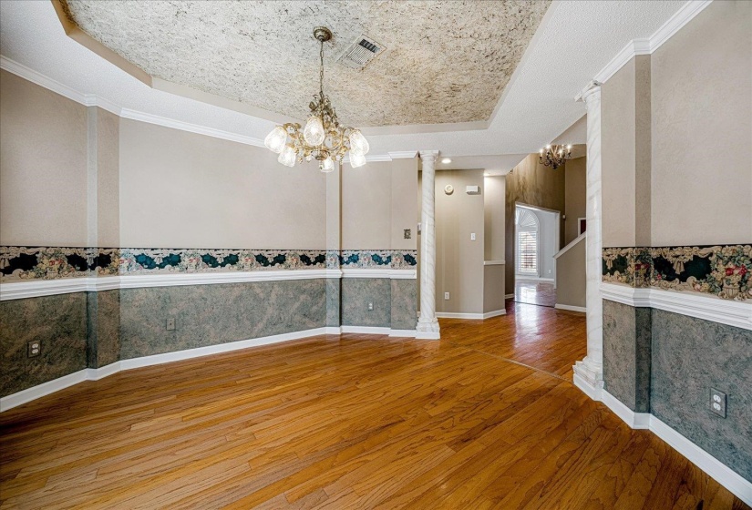Unfurnished dining area featuring wallpapered walls, a chandelier, crown molding, a raised ceiling, and hardwood / wood-style flooring