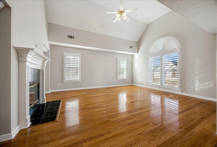 Unfurnished living room with light wood-type flooring, a fireplace, a ceiling fan, and high vaulted ceiling