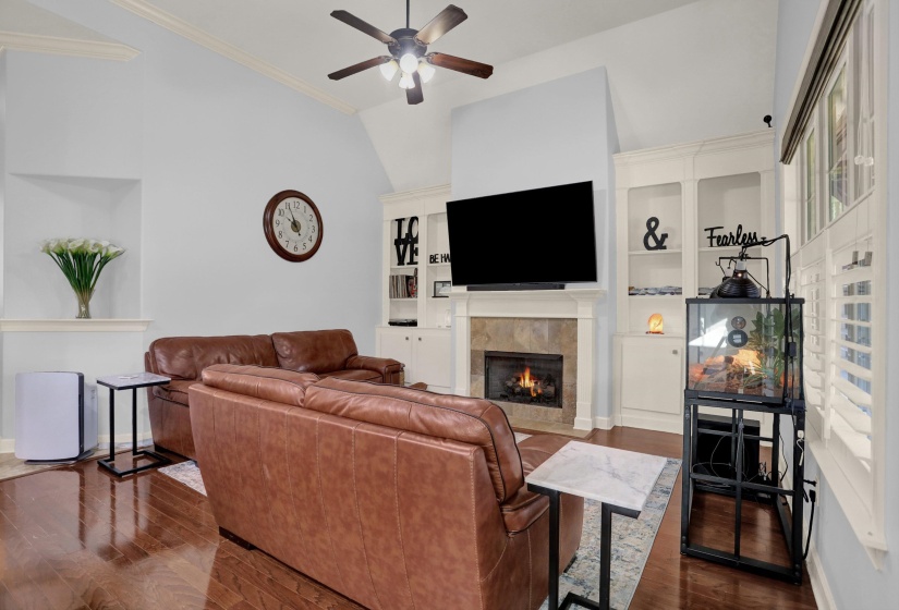 Living room with a tile fireplace, dark wood-style floors, ornamental molding, vaulted ceiling, and ceiling fan