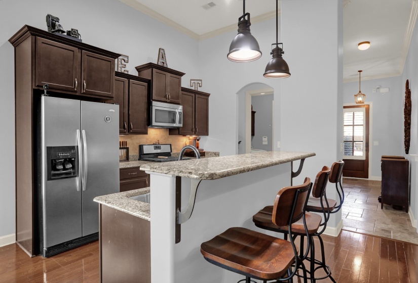 Kitchen featuring dark brown cabinets, crown molding, stainless steel appliances, a kitchen island with sink, and a breakfast bar
