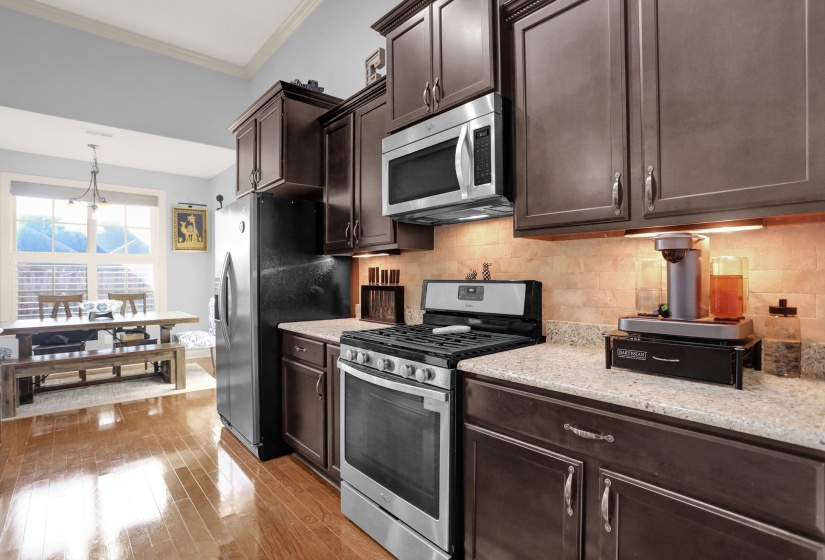 Kitchen with dark brown cabinetry, stainless steel appliances, ornamental molding, light wood-style floors, and decorative light fixtures