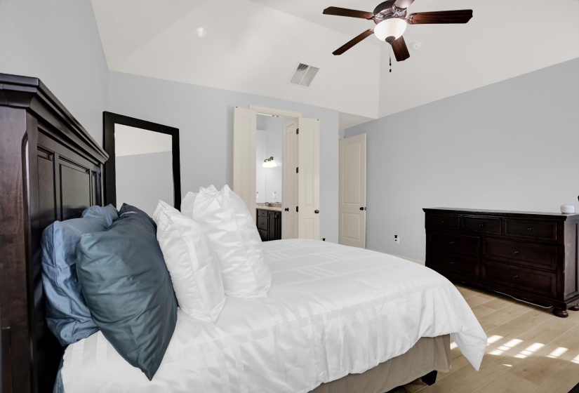 Bedroom with lofted ceiling, light wood finished floors, ceiling fan, and ensuite bath