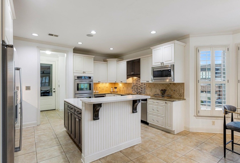 Kitchen with a kitchen breakfast bar, ornamental molding, backsplash, appliances with stainless steel finishes, and white cabinetry
