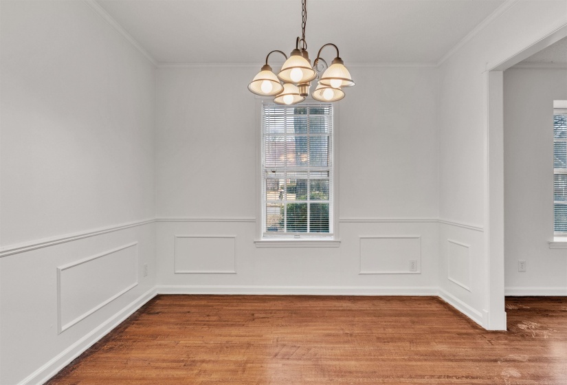 Unfurnished dining area with a chandelier, wood finished floors, ornamental molding, a decorative wall, and a wainscoted wall