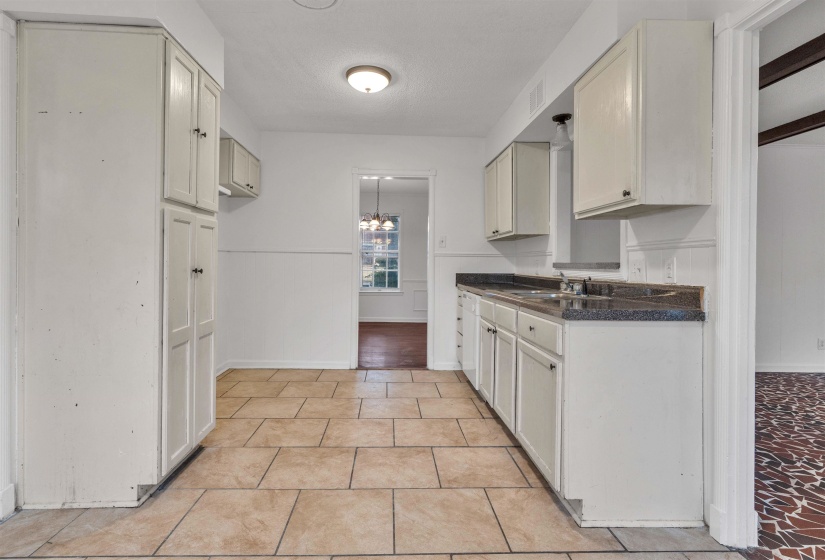 Kitchen featuring a wainscoted wall, dark countertops, a chandelier, white cabinetry, and a decorative wall