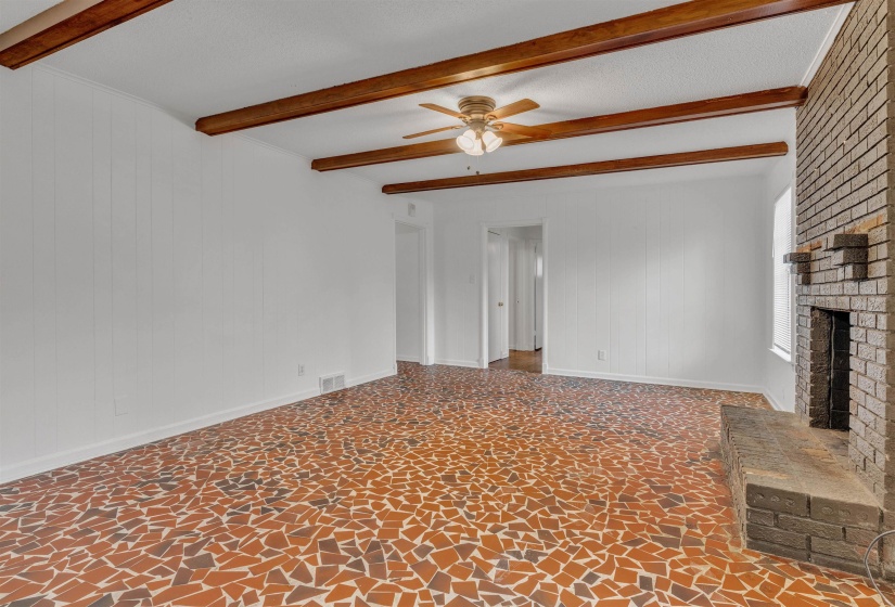Unfurnished living room featuring a fireplace, beamed ceiling, wooden walls, ceiling fan, and a textured ceiling