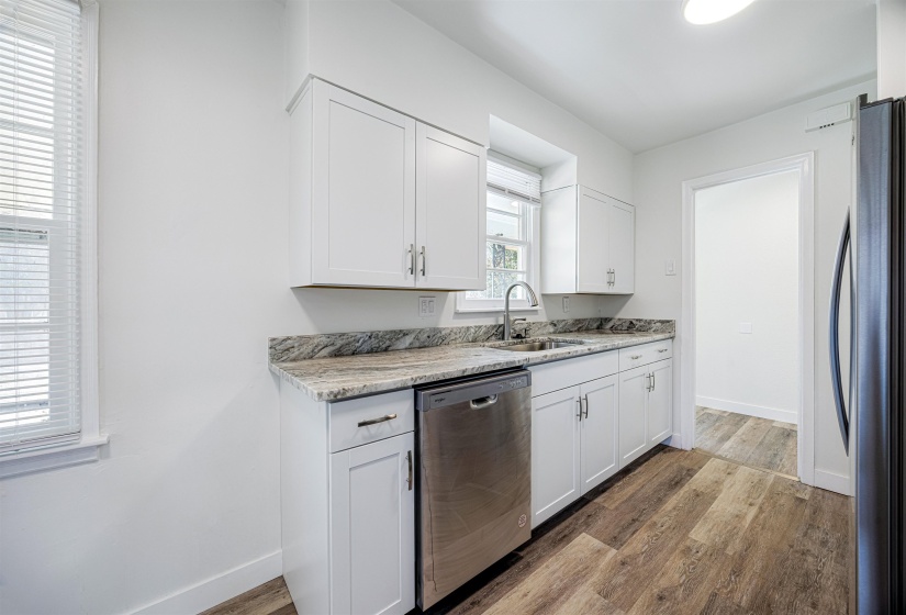 Kitchen with appliances with stainless steel finishes, light stone counters, light wood-type flooring, and white cabinets