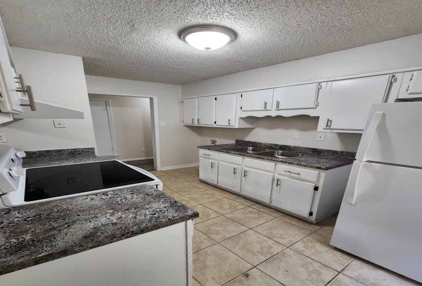 Kitchen with a textured ceiling, light tile patterned floors, white appliances, and white cabinetry