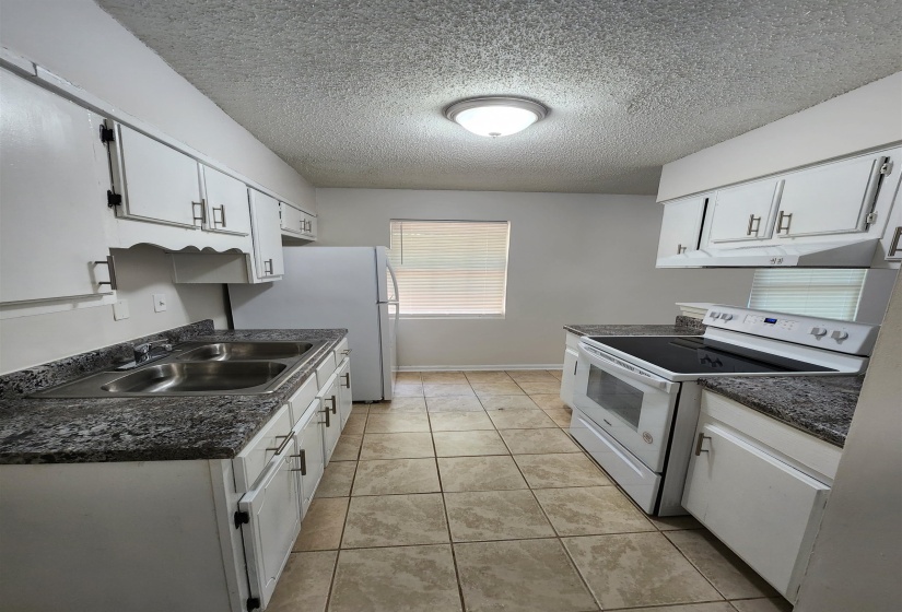 Kitchen with white cabinets, white appliances, sink, light tile patterned flooring, and a textured ceiling