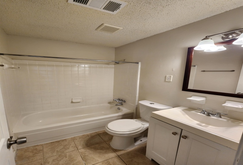 Full bathroom with tile patterned flooring, toilet, tub / shower combination, vanity, and a textured ceiling