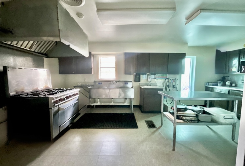 Kitchen featuring ventilation hood, light countertops, stainless steel range with gas stovetop, and light flooring