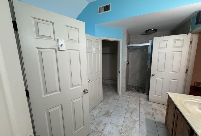 Full bathroom featuring vanity, a stall shower, a walk in closet, and vaulted ceiling