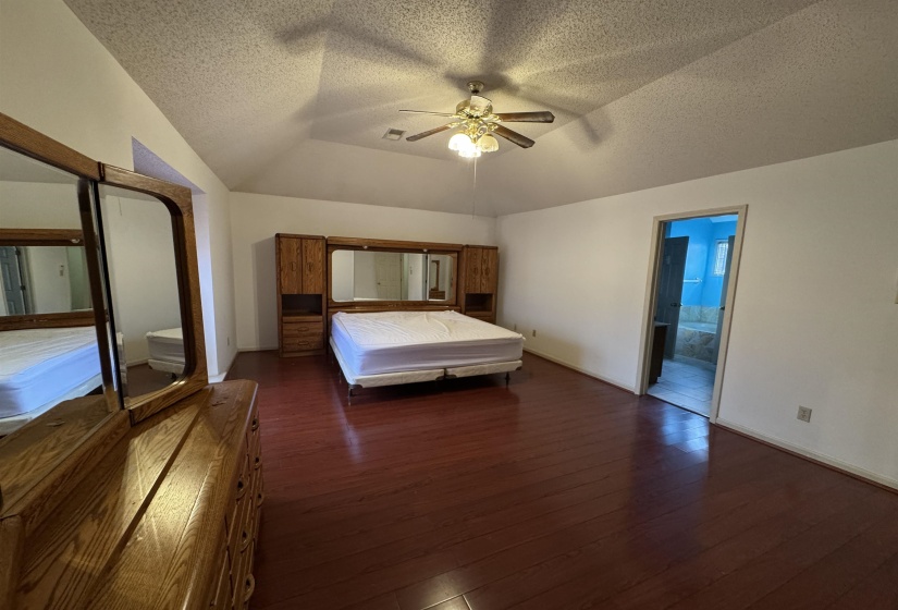 Bedroom featuring dark wood finished floors, lofted ceiling, connected bathroom, a ceiling fan, and a textured ceiling