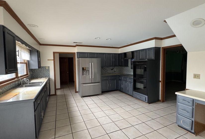 Kitchen featuring black appliances, ornamental molding, tasteful backsplash, and light tile patterned floors
