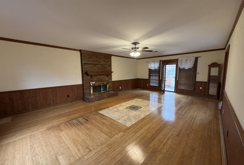Unfurnished living room with wainscoting, light wood finished floors, a fireplace, wooden walls, and ceiling fan