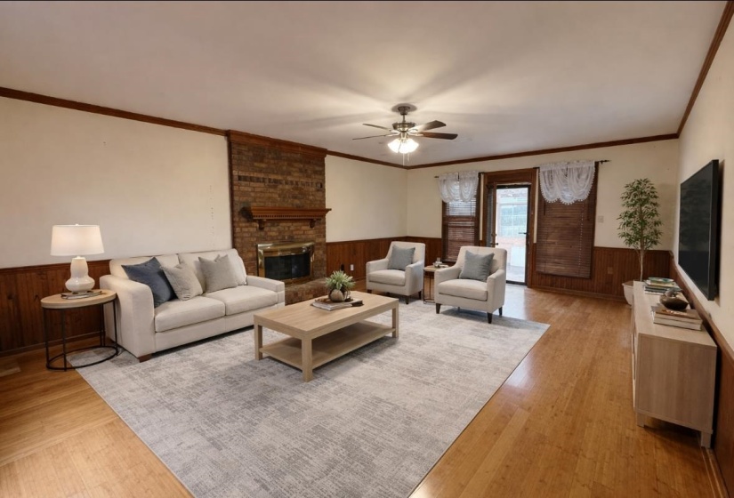 Living room featuring wainscoting, wood walls, ceiling fan, crown molding, and a fireplace