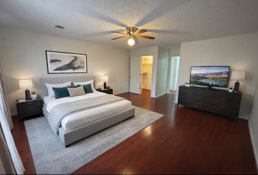 Bedroom featuring a walk in closet, dark wood-style floors, a ceiling fan, and a textured ceiling