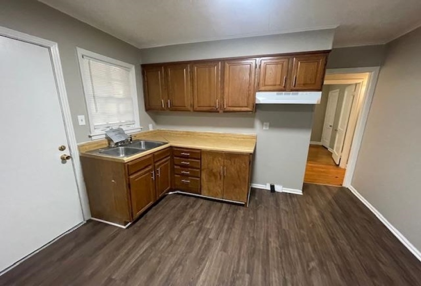 Kitchen featuring light countertops, brown cabinetry, dark wood-type flooring, and under cabinet range hood
