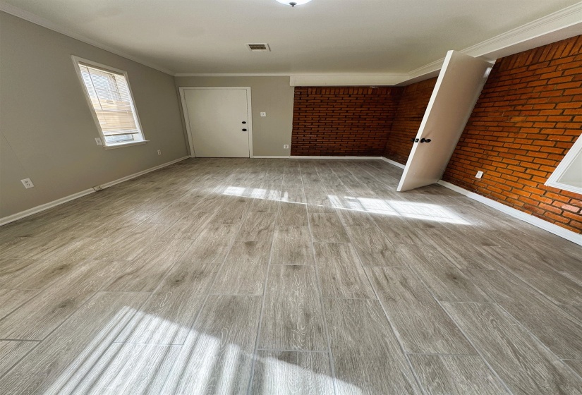 Unfurnished room featuring brick wall, light wood-type flooring, and ornamental molding