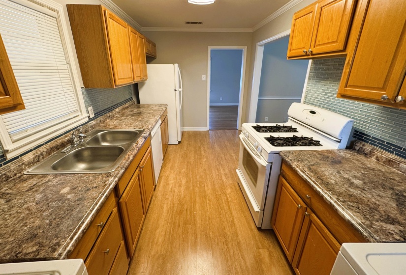 Kitchen featuring white appliances, brown cabinetry, light wood-style floors, ornamental molding, and decorative backsplash