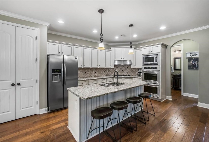 Kitchen with arched walkways, stainless steel appliances, a breakfast bar area, light stone countertops, and a center island with sink