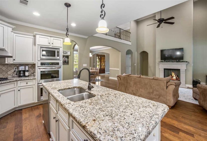 Kitchen featuring dark wood finished floors, white cabinetry, arched walkways, a warm lit fireplace, and light stone counters