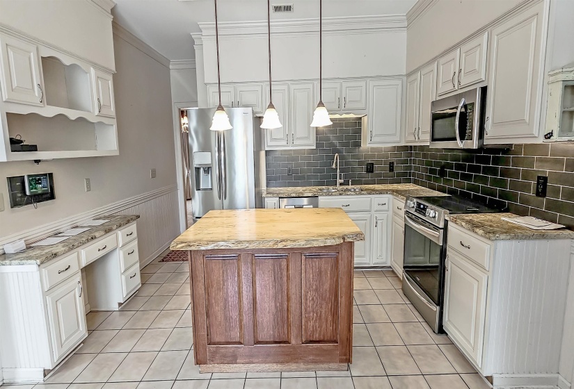 Kitchen featuring decorative light fixtures, appliances with stainless steel finishes, light stone counters, backsplash, and a center island