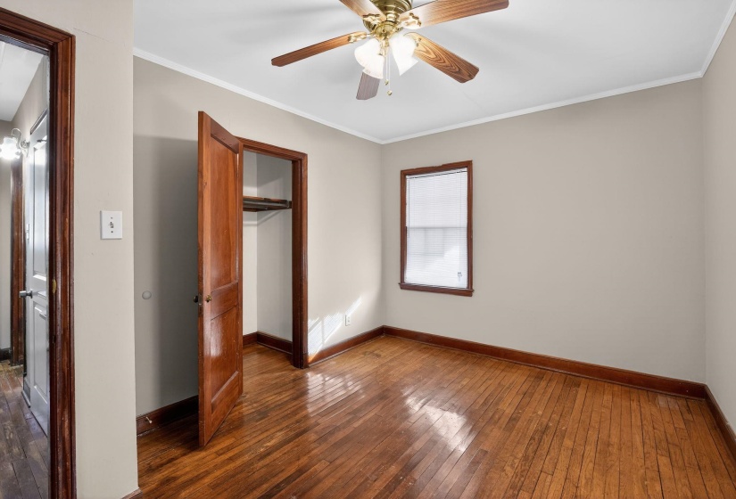 Unfurnished bedroom with wood-type flooring, crown molding, a ceiling fan, and a closet