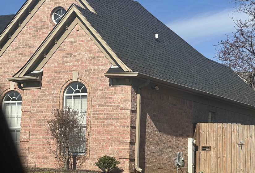 View of side of home with brick siding, a gate, and a shingled roof