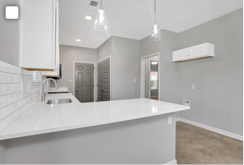 Kitchen with a peninsula, light stone counters, white cabinets, pendant lighting, and decorative backsplash