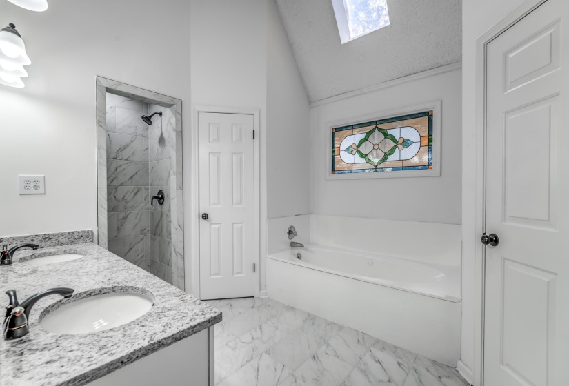 Bathroom with a skylight, a garden tub, double vanity, light marble finish flooring, and vaulted ceiling