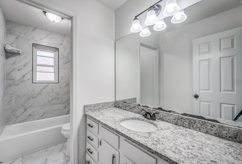 Bathroom featuring vanity, shower / tub combination, light marble finish floors, and a textured ceiling